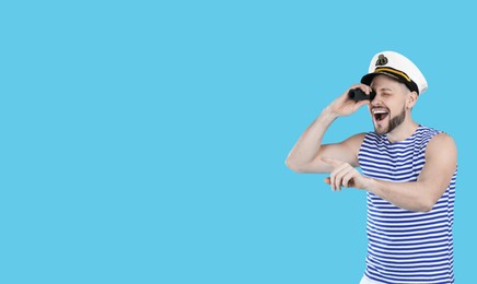Photo of Sailor looking through monocular and pointing on light blue background