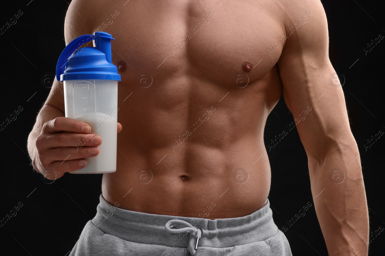 Photo of Young man with muscular body holding shaker of protein on black background, closeup