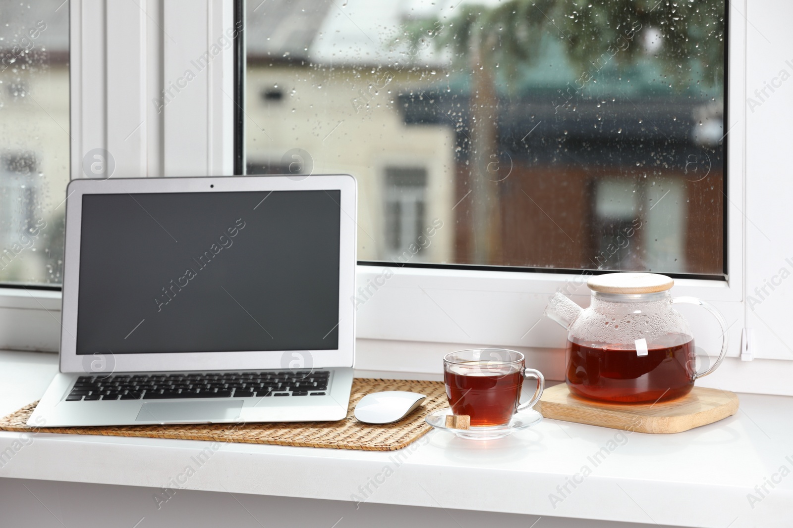 Photo of Modern laptop and tea on white sill near window