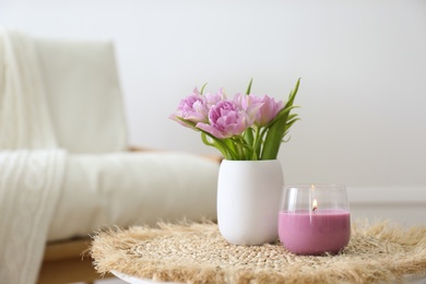 Vase with beautiful flowers and burning candle on table indoors, space for text. Interior elements