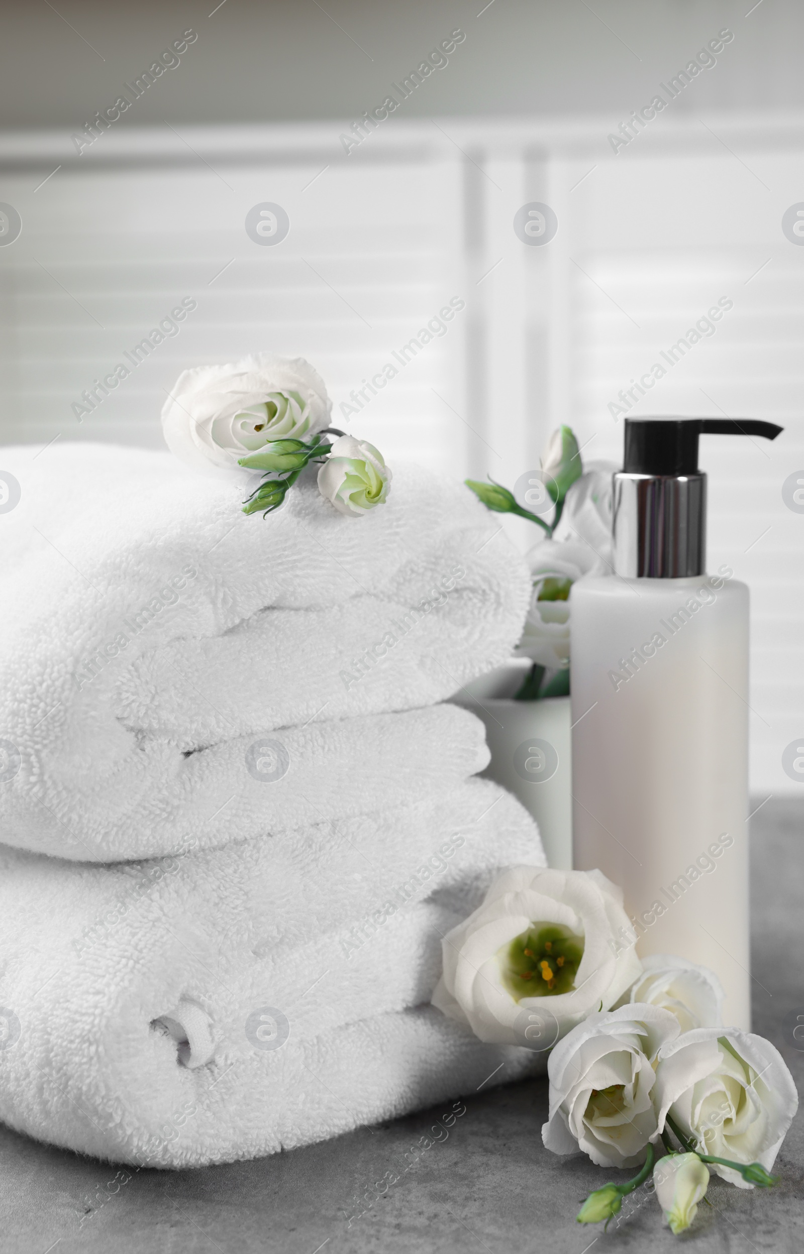 Photo of Cosmetic product, folded towels and flowers on gray marble table