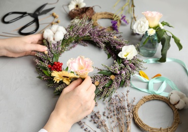 Florist making beautiful autumnal wreath with heather flowers at light grey table, closeup