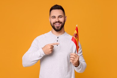 Young man holding flag of Spain on orange background