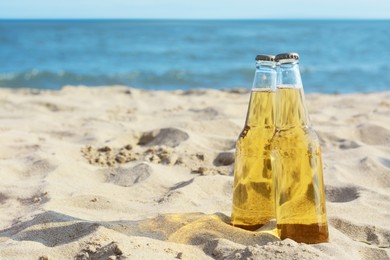 Photo of Bottles of cold beer on sandy beach near sea, space for text