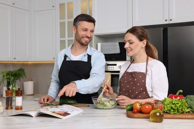 Photo of Happy couple reading recipe in culinary magazine while cooking at home