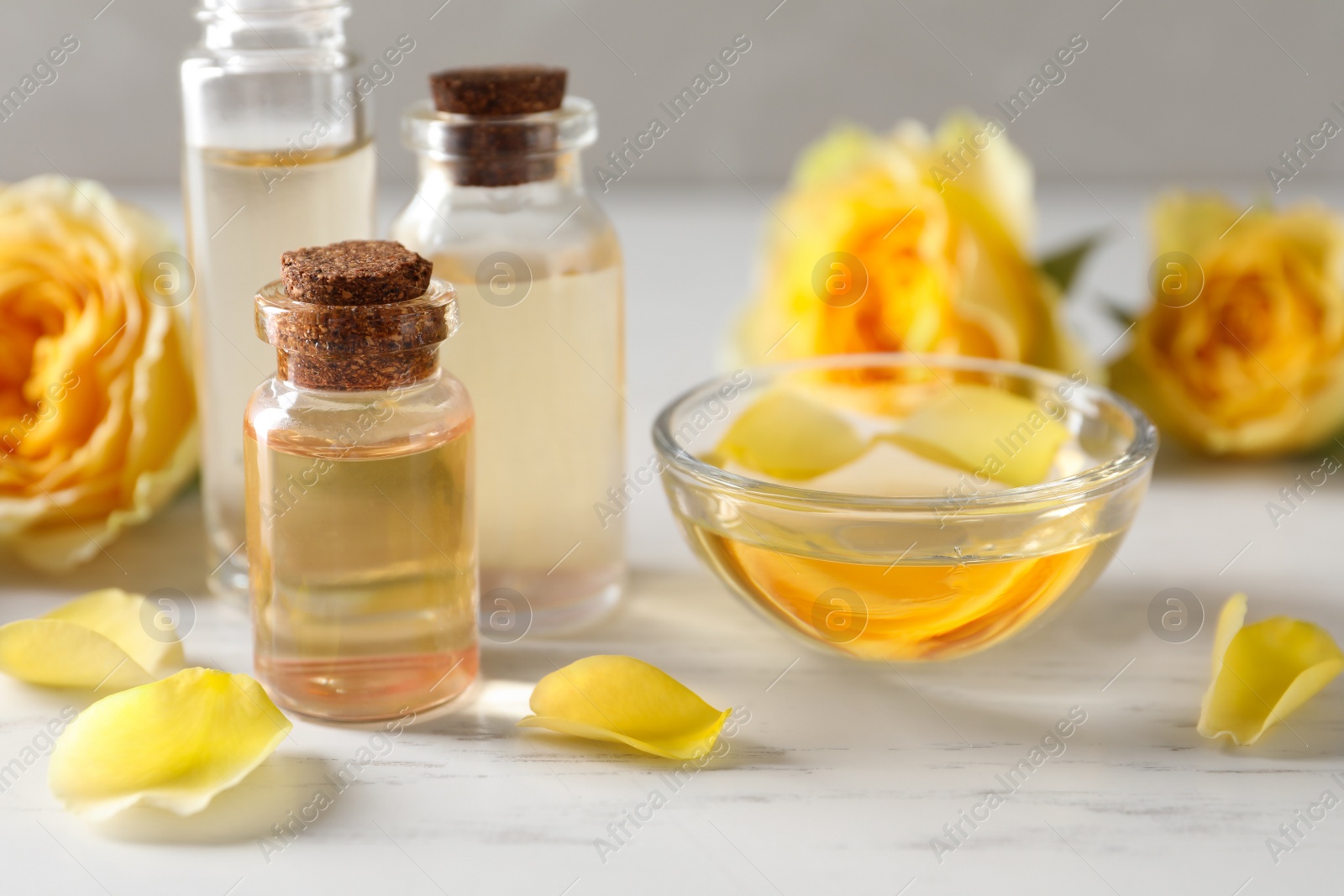 Photo of Bottles and bowl of rose essential oil and fresh flowers on white table