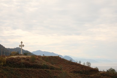 Photo of Picturesque view of beautiful sea, mountains and old cross under cloudy sky