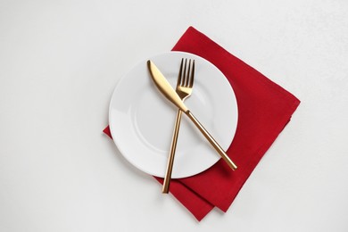 Photo of Clean plate and golden cutlery on white table, flat lay