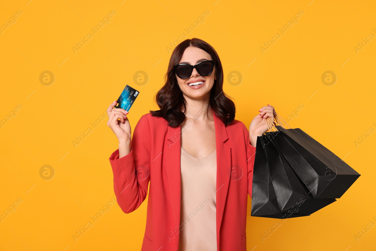 Photo of Beautiful young woman with paper shopping bags and credit card on yellow background