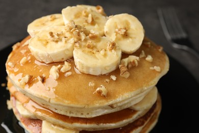 Photo of Delicious pancakes with bananas, walnuts and honey on dark table, closeup