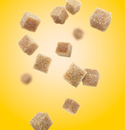 Image of Brown cane sugar cubes falling on golden gradient background