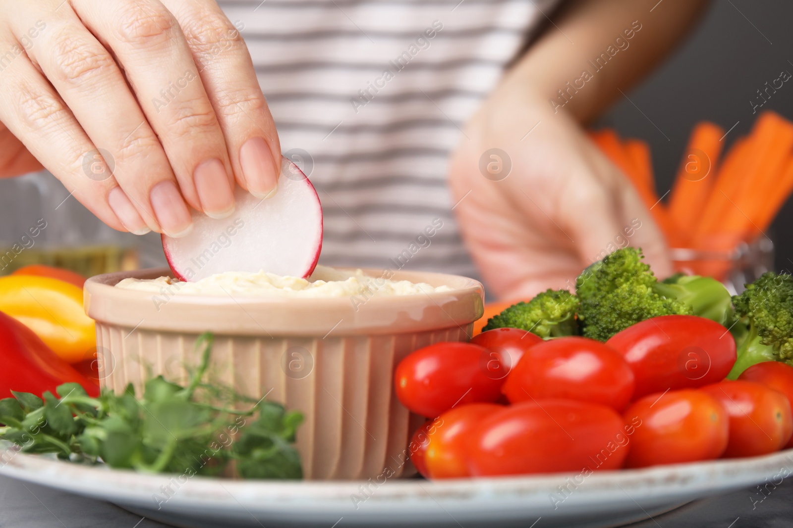 Photo of Woman dipping slice of radish into hummus at table, closeup