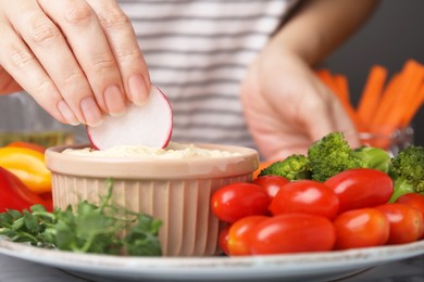 Woman dipping slice of radish into hummus at table, closeup