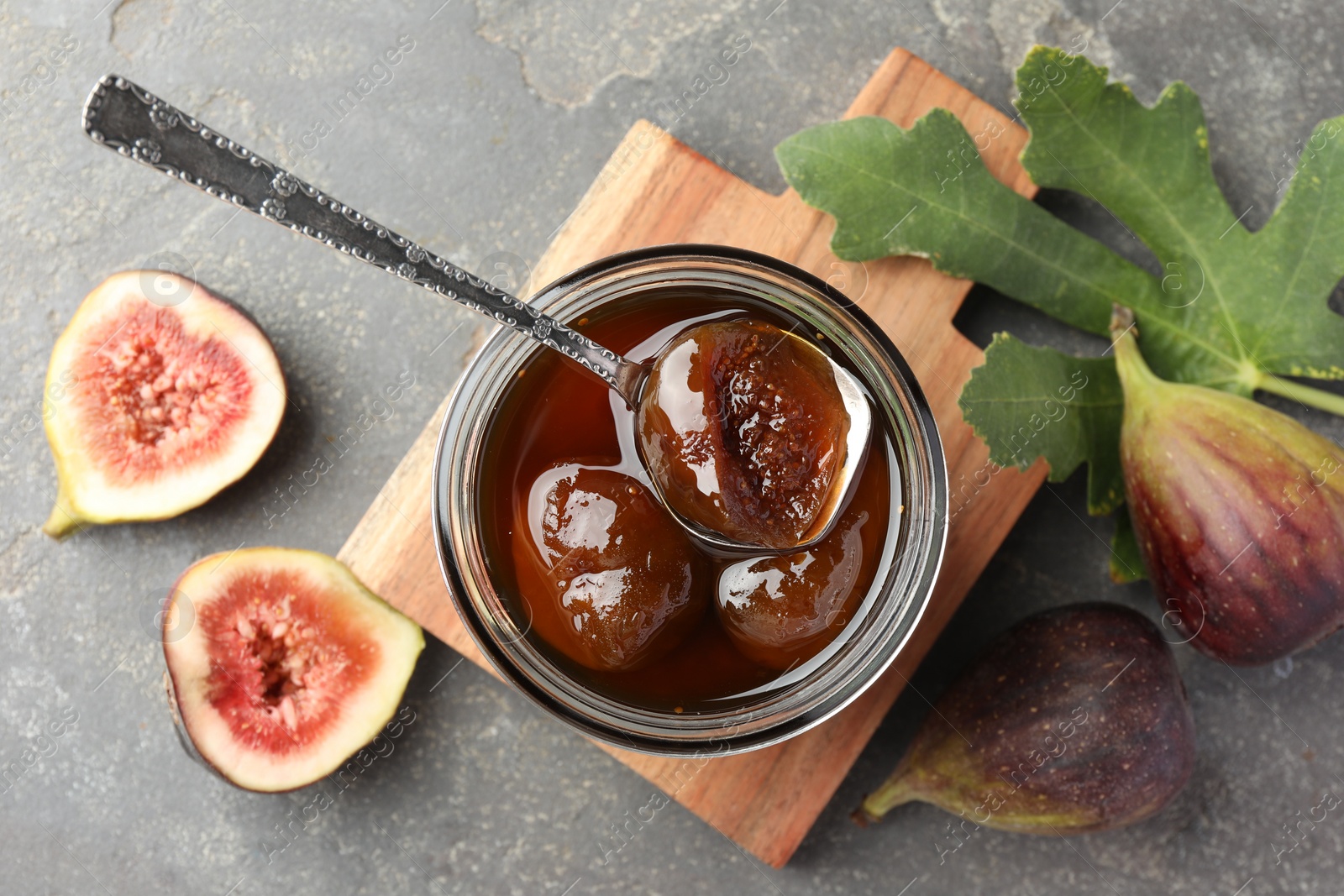 Photo of Jar of tasty sweet jam, fresh figs and green leaf on grey table, flat lay