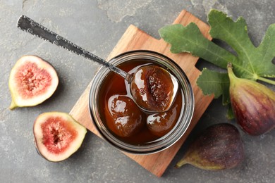 Jar of tasty sweet jam, fresh figs and green leaf on grey table, flat lay