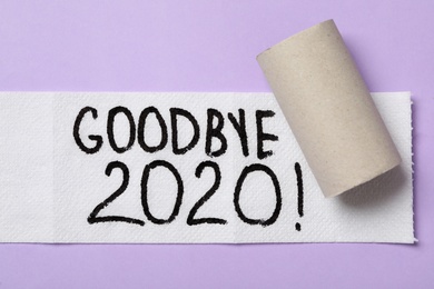 Photo of Toilet paper with text Goodbye 2020 on lilac background, flat lay