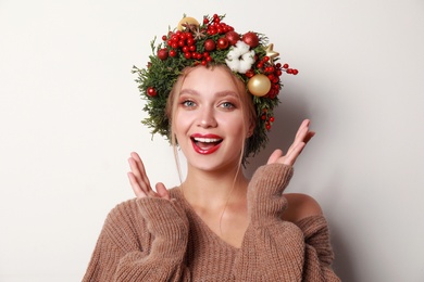 Beautiful young woman wearing Christmas wreath on white background