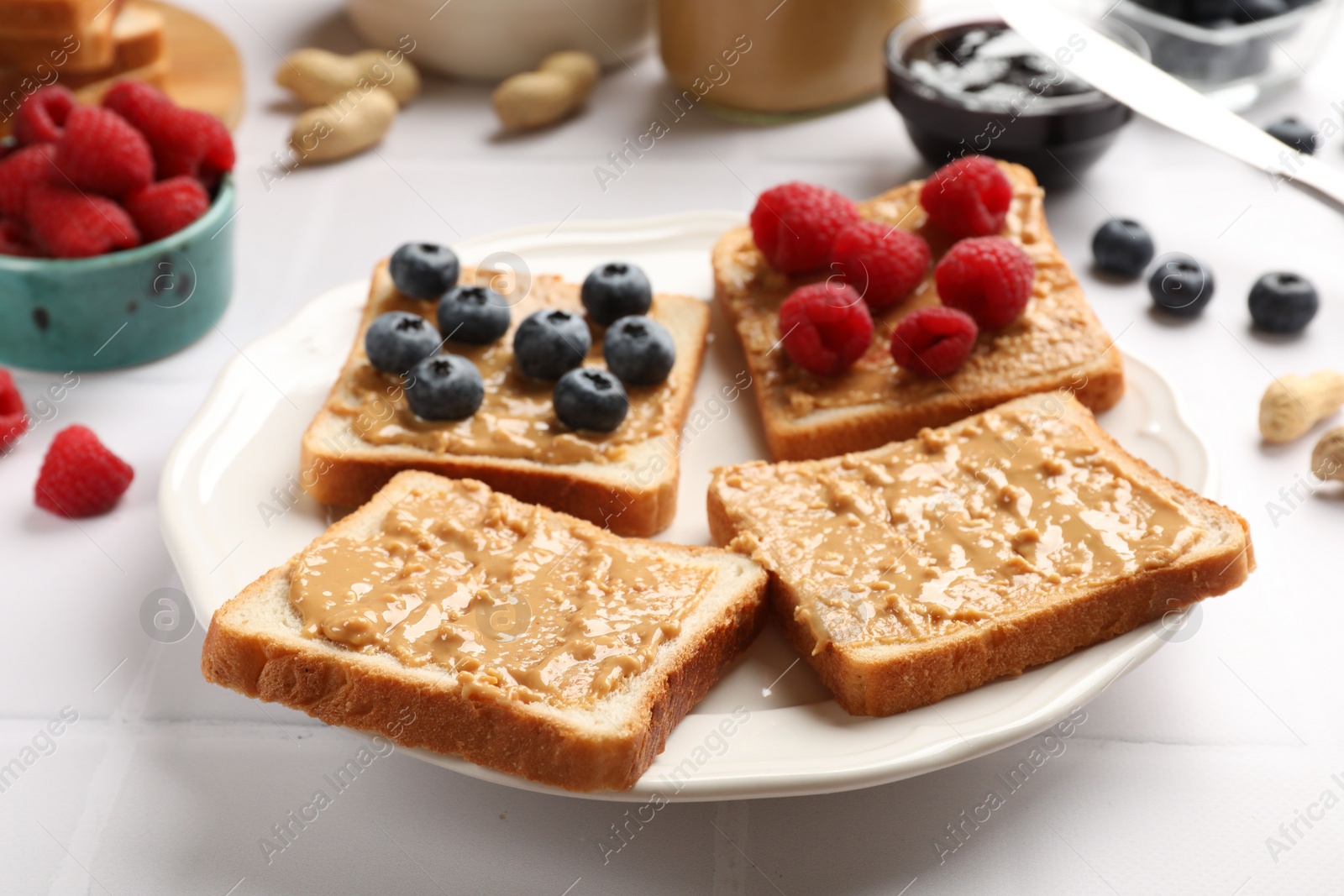 Photo of Delicious toasts with peanut butter, raspberries and blueberries on white table, closeup