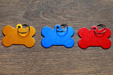 Color metal pet tags in shape of bones with ring on wooden table, flat lay. Space for text