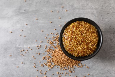 Photo of Bowl of whole grain mustard and seeds on grey table, top view. Space for text