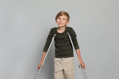 Photo of Portrait of happy boy with crutches on grey background