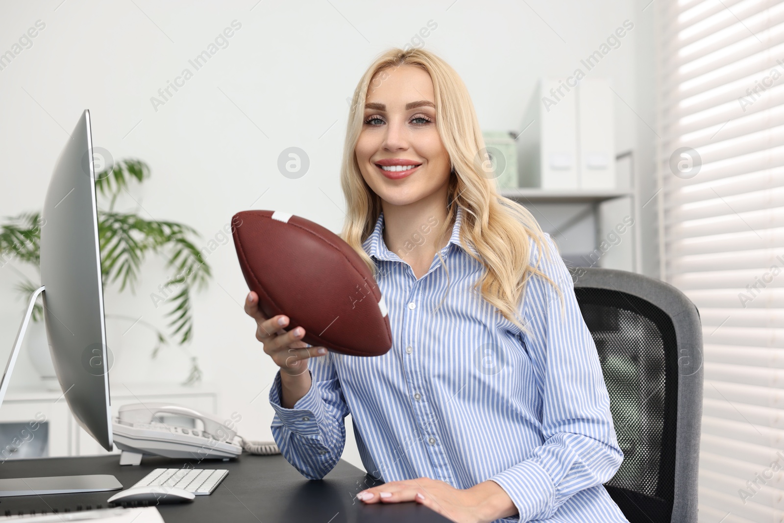 Photo of Happy woman with american football ball at table in office