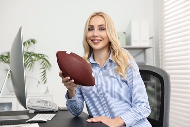 Happy woman with american football ball at table in office