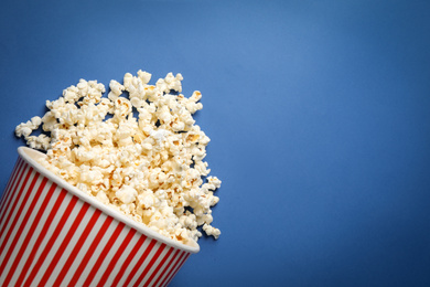 Photo of Overturned paper bucket with delicious popcorn on blue background, top view. Space for text