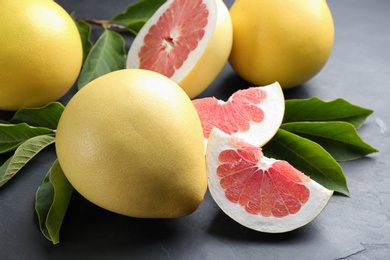 Photo of Fresh cut and whole pomelo fruits on black slate table, closeup