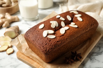 Photo of Delicious gingerbread cake with almond petals on white marble table