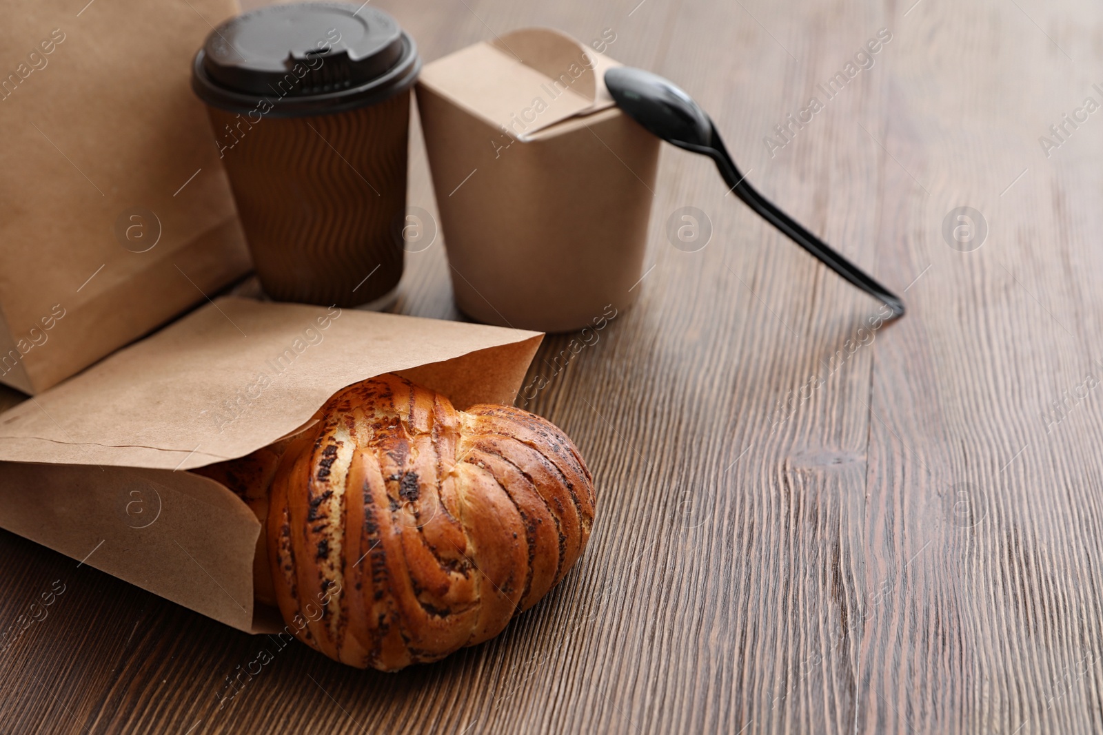 Photo of Bun in paper bag and takeaway food on wooden table. Space for text
