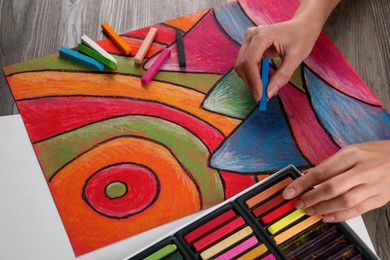 Photo of Woman drawing abstract mountain landscape with soft pastel at wooden table, above view