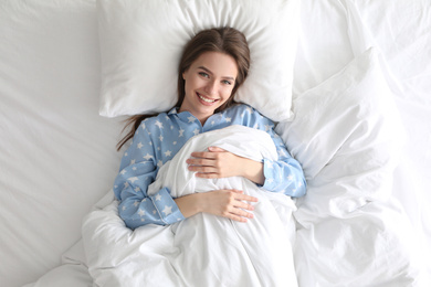 Young woman lying on comfortable pillow in bed at home, top view