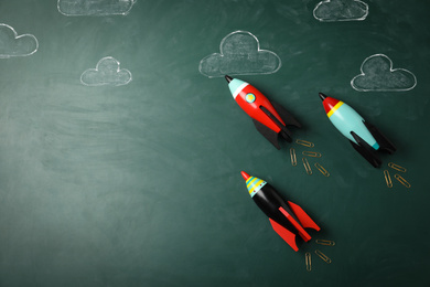 Photo of Bright toy rockets and drawings on chalkboard, flat lay with space for text. Back to school