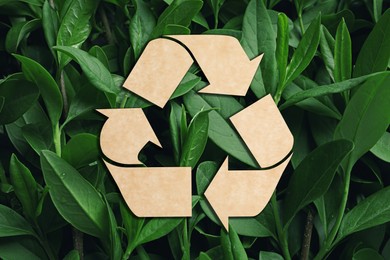 Image of Recycling symbol cut out of kraft paper and fresh green leaves on background