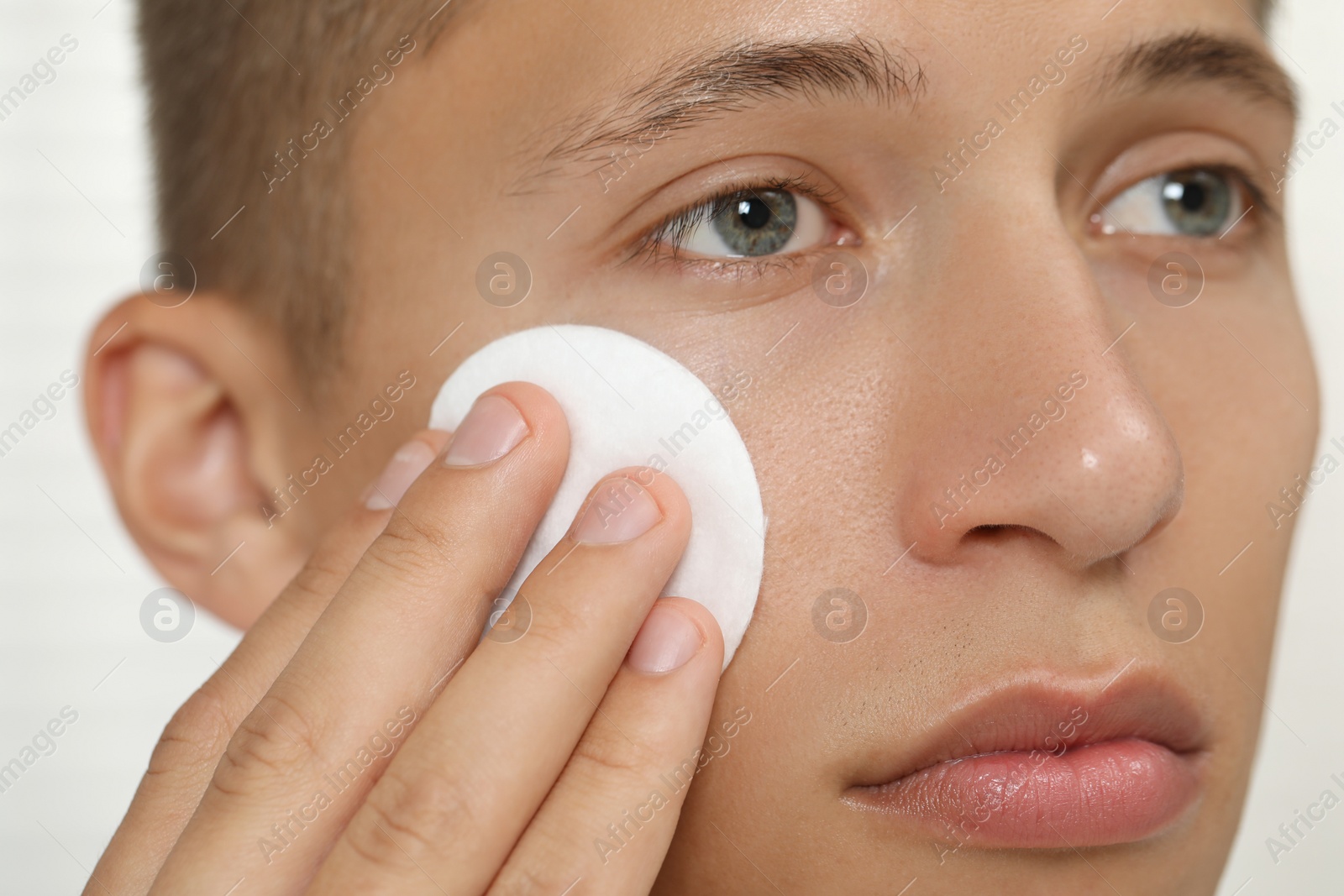 Photo of Handsome man cleaning face with cotton pad, closeup