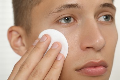 Handsome man cleaning face with cotton pad, closeup