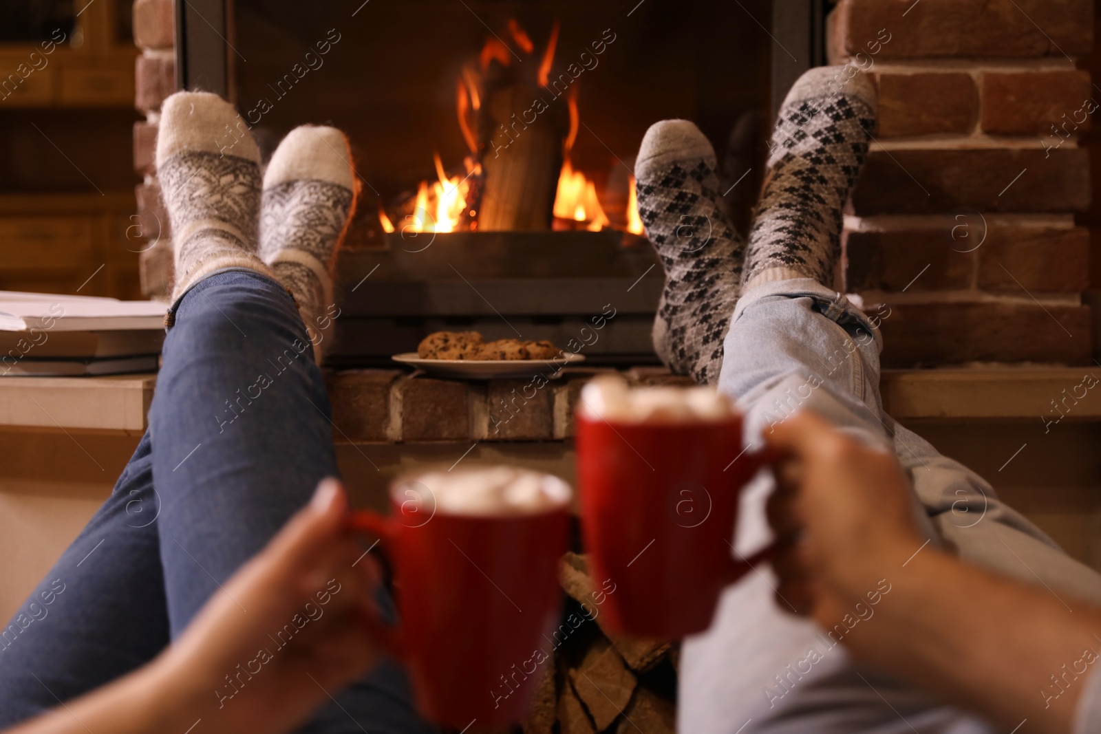 Photo of Couple with cups of delicious cocoa resting near fireplace at home, closeup. Winter vacation