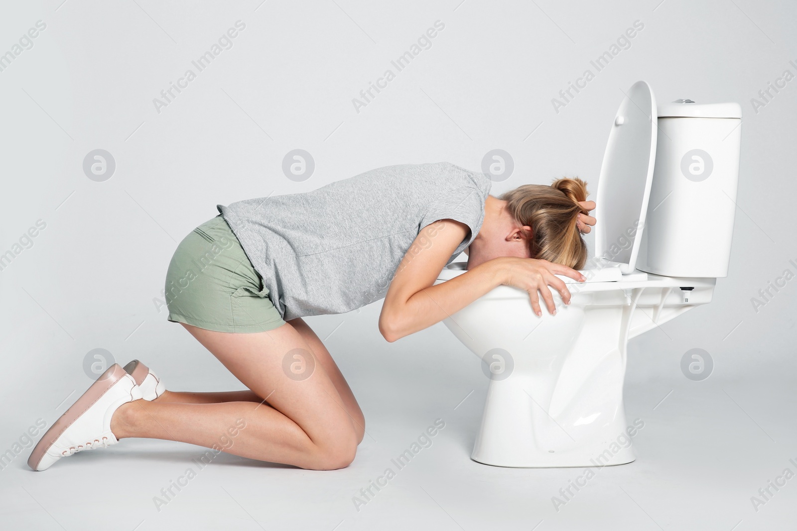 Photo of Young woman vomiting in toilet bowl on gray background