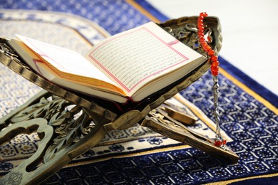 Photo of Rehal with open Quran and Misbaha on Muslim prayer rug, closeup