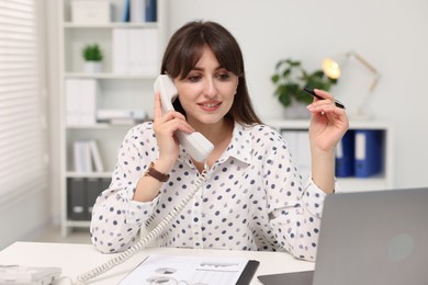 Smiling secretary talking on telephone at table in office