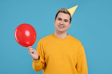 Young man with party hat and balloon on light blue background