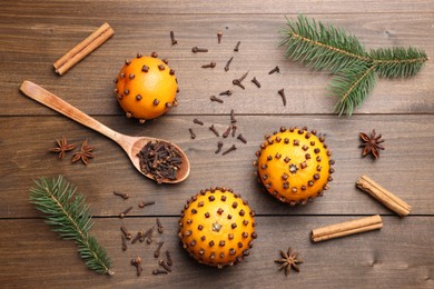 Pomander balls made of tangerines with cloves and fir branches on wooden table, flat lay