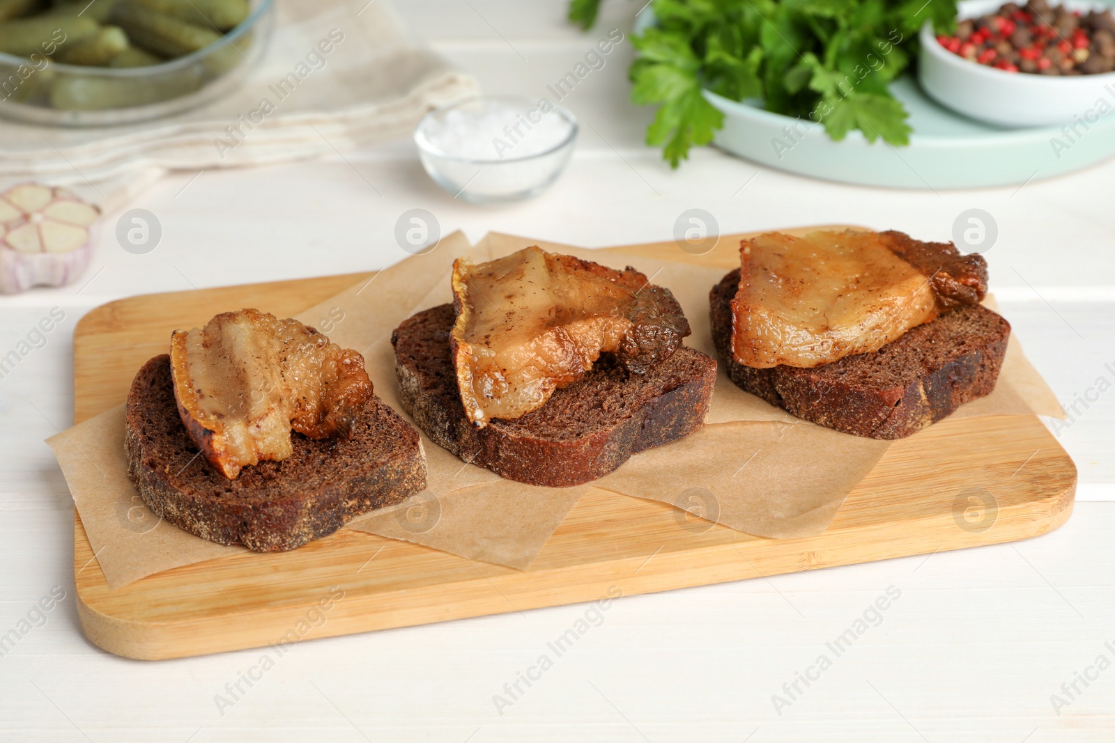 Photo of Rye bread with tasty fried cracklings on white wooden table. Cooked pork lard