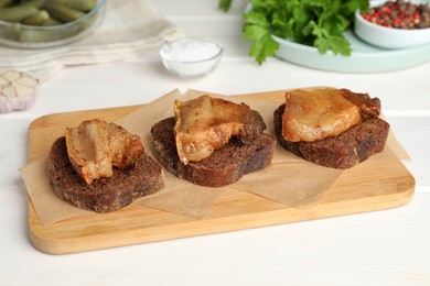 Photo of Rye bread with tasty fried cracklings on white wooden table. Cooked pork lard