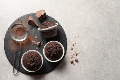 Delicious chocolate muffins and sieve with cocoa powder on light table, top view. Space for text