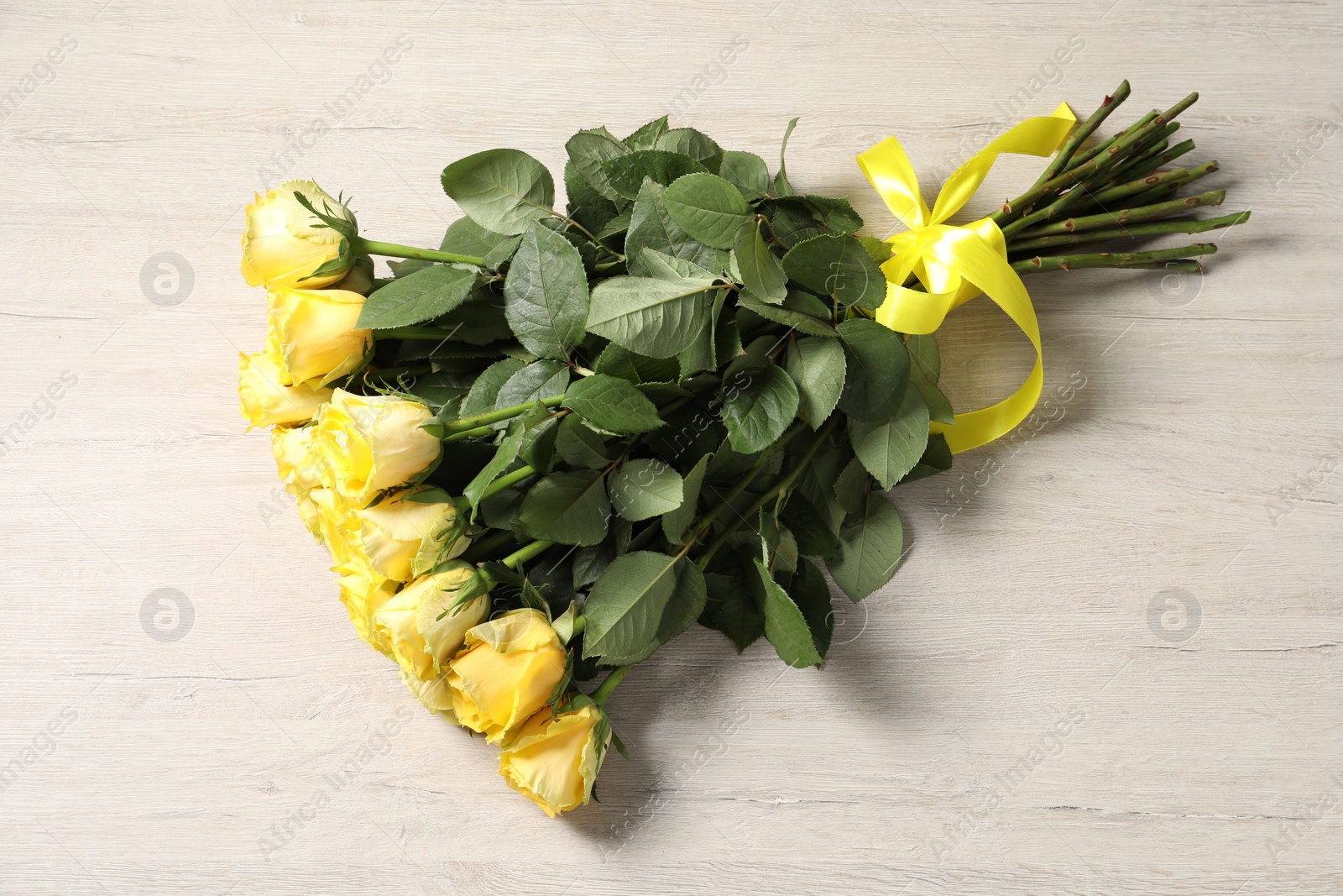 Photo of Beautiful bouquet of yellow roses on wooden table, top view