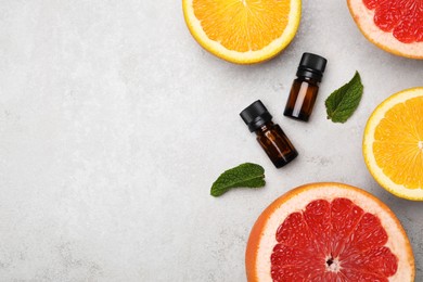 Bottles of citrus essential oils and fresh fruits on light table, flat lay. Space for text