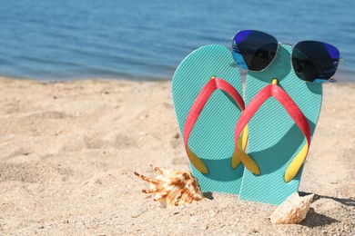 Photo of Stylish flip flops, sunglasses and seashells on sandy beach, space for text