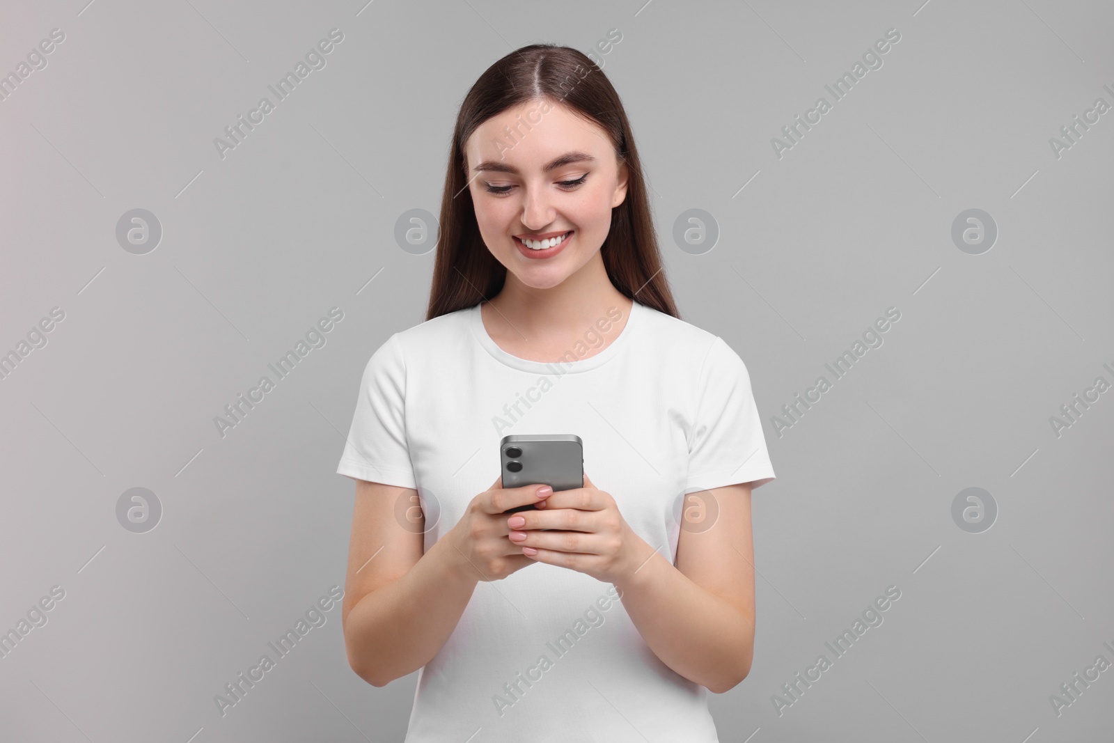 Photo of Smiling woman using smartphone on light grey background